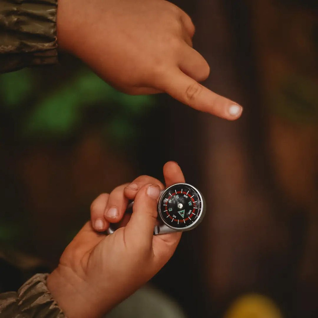 Hand holding a compass with another hand pointing in a direction.